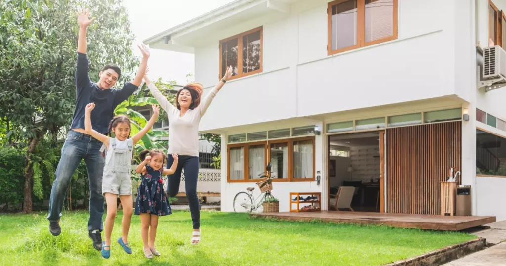 A group of people jumping in the grass in front of a house 