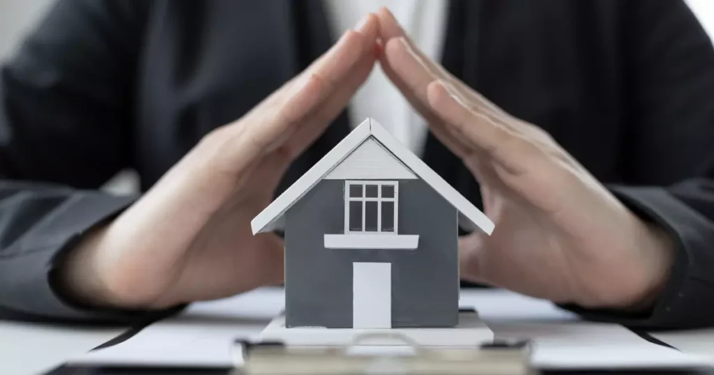 A person's hands covering a small house